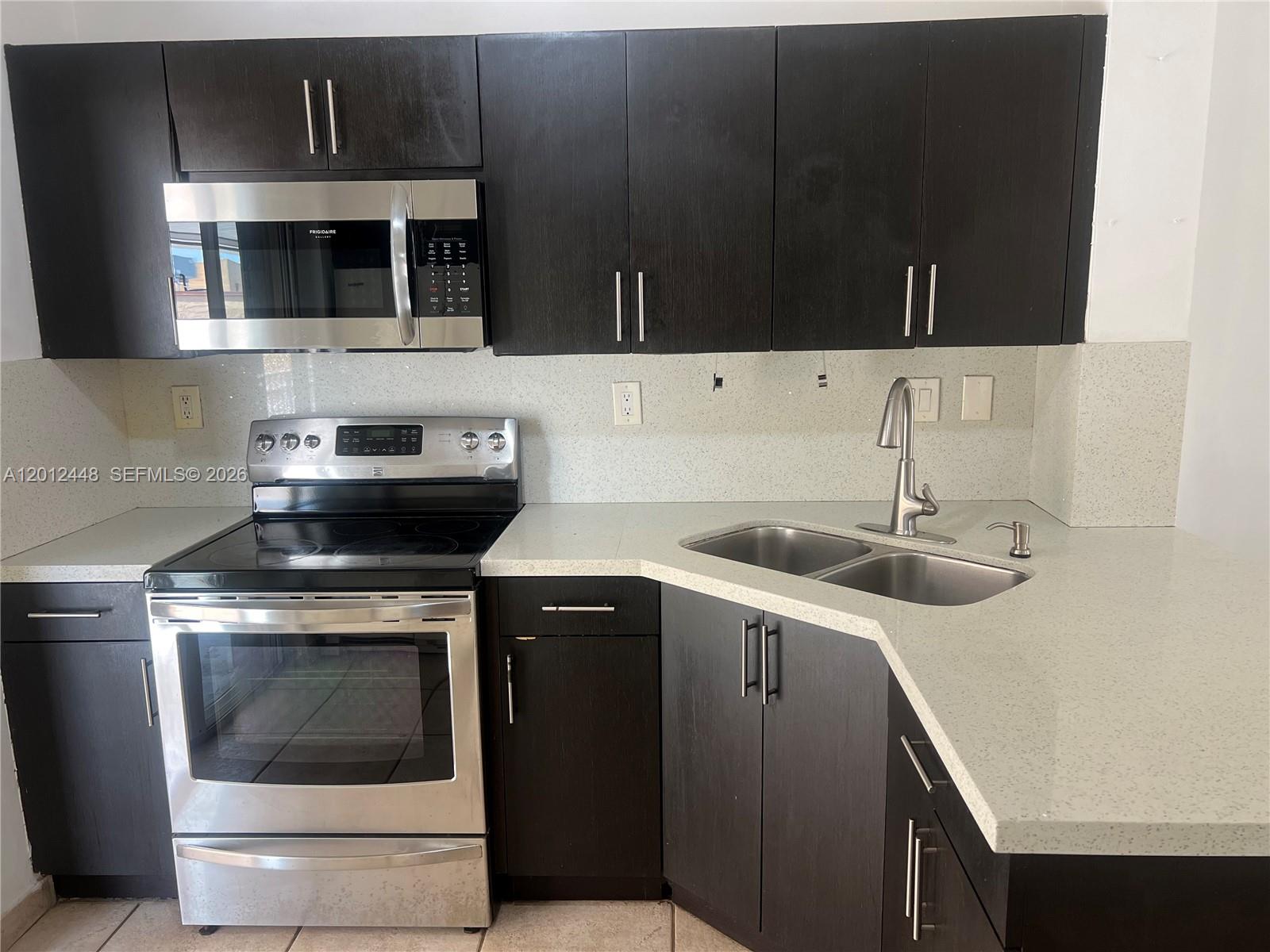 A bright, minimalist room features white walls, light gray tile flooring, and a staircase railing — 2425 W 76th St # 207, Hialeah FL 33016, HIALEAH, FL