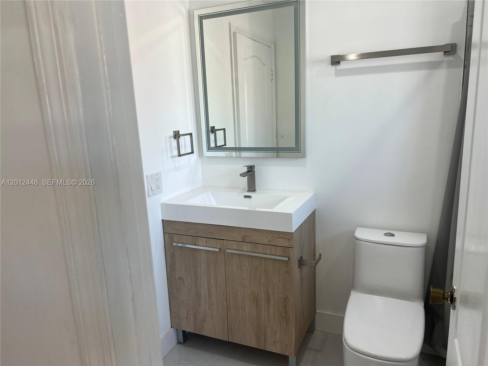 A staircase with wooden handrails leads down to a closed door in a white room — 2425 W 76th St # 207, Hialeah FL 33016, HIALEAH, FL