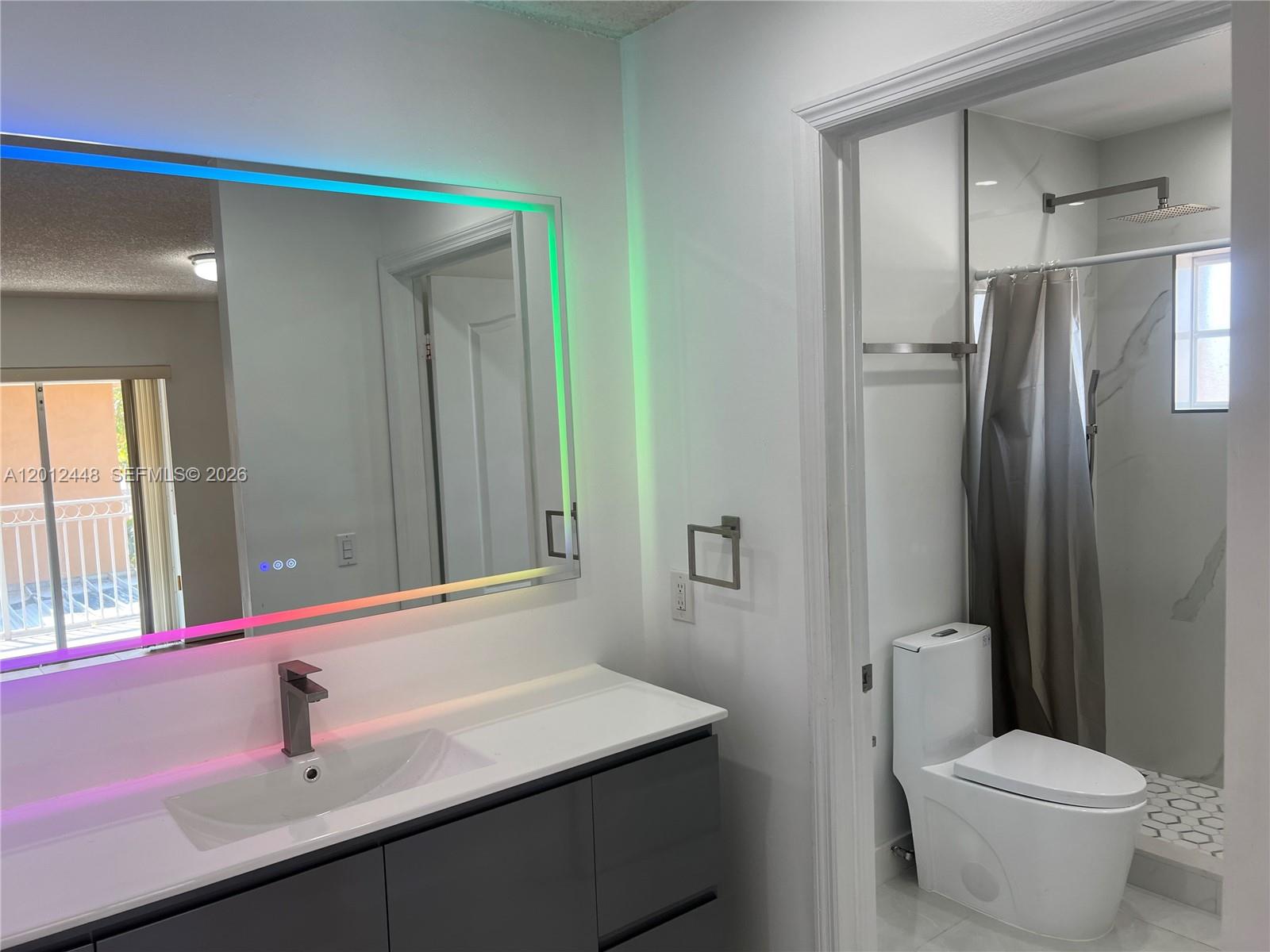 A small bathroom features a wood-toned vanity, a rectangular sink, and a wall-mounted mirror — 2425 W 76th St # 207, Hialeah FL 33016, HIALEAH, FL