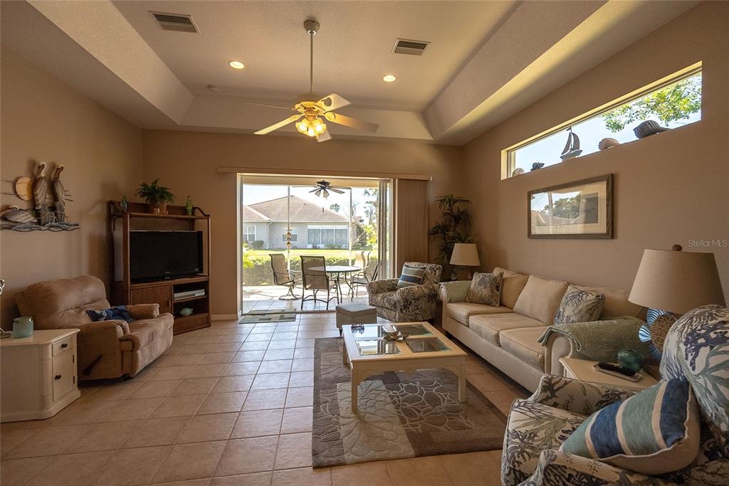 A living room with tile floors, a tray ceiling, and a sliding door to a patio — 8363 SAGO COURT, ENGLEWOOD, FL