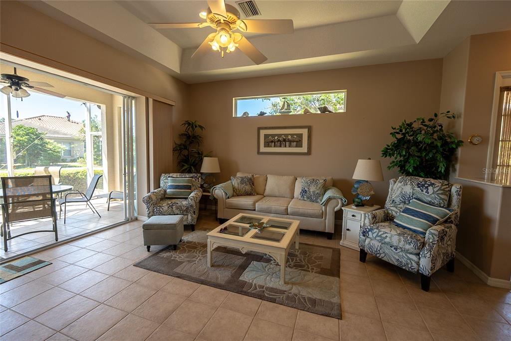 A living room with tile floors, a beige sofa, two patterned armchairs, and sliding glass doors — 8363 SAGO COURT, ENGLEWOOD, FL