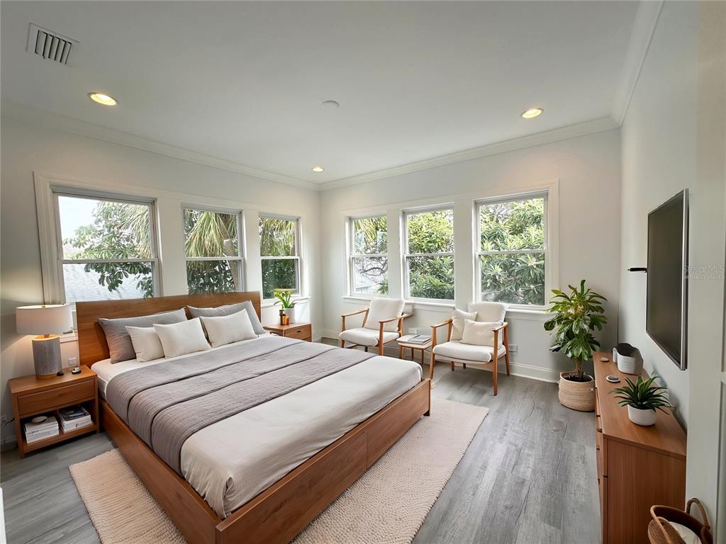 A bedroom features a wooden bed frame, gray flooring, and multiple windows overlooking trees — 3025 W NORTH A STREET, TAMPA, FL