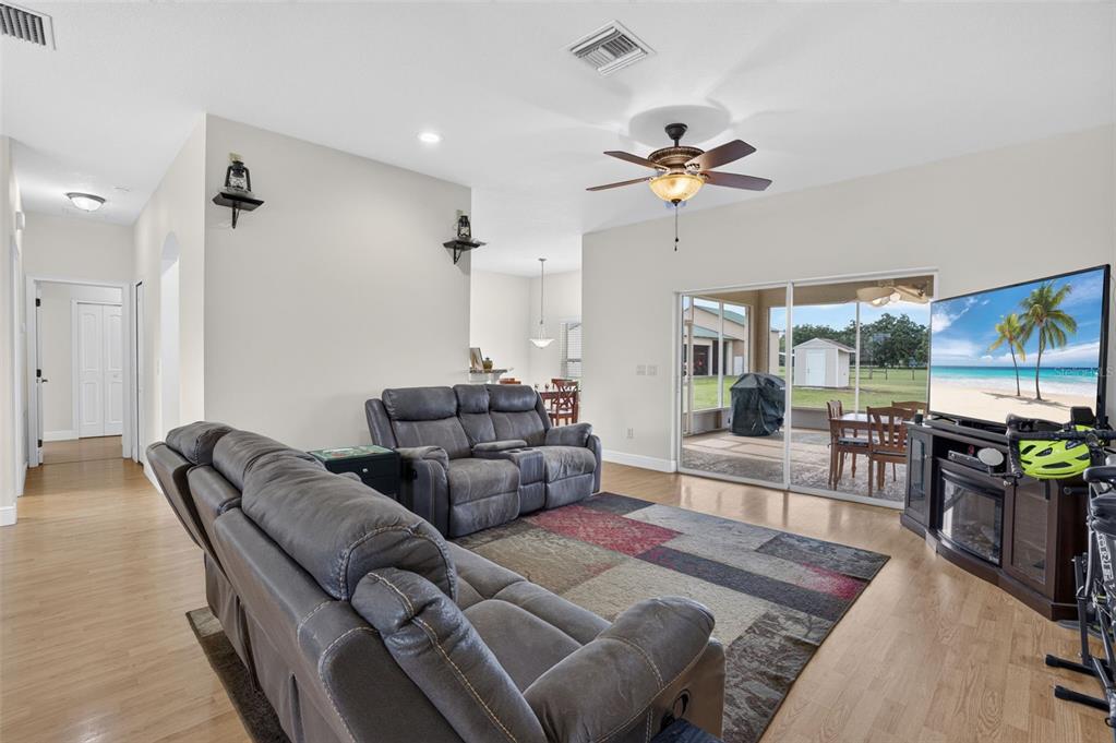 A living room features gray reclining sofas, a patterned area rug, and sliding glass doors — 2440 CR 546, BUSHNELL, FL