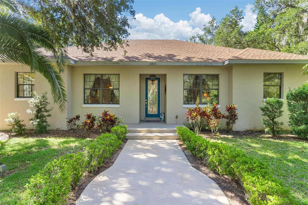 A single-story house with a beige stucco exterior, a brown roof, and a concrete walkway — 26833 ANDERSON RANCH ROAD, YALAHA, FL