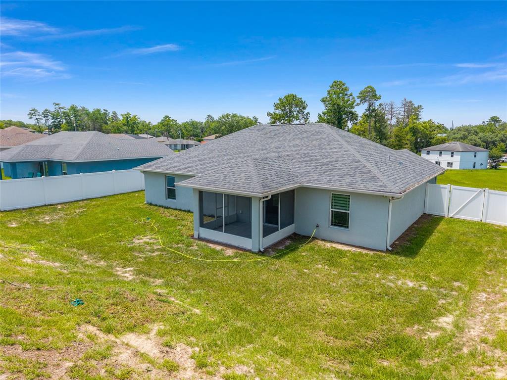 The back exterior of a light-colored house features a screened-in porch and a white fence — 15017 SW 46TH CIRCLE, OCALA, FL