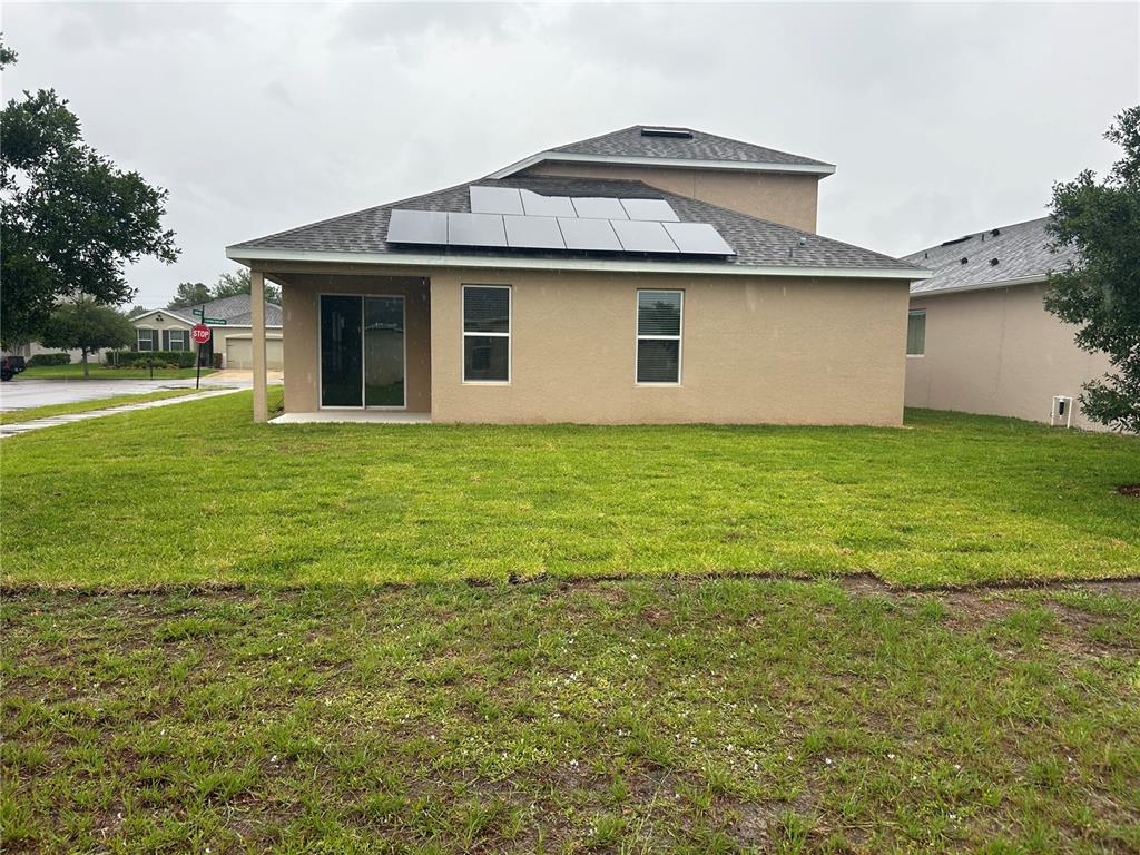 The rear exterior of a tan house features a sliding glass door and solar panels — 720 E VICTORIA TRAILS BOULEVARD, DELAND, FL