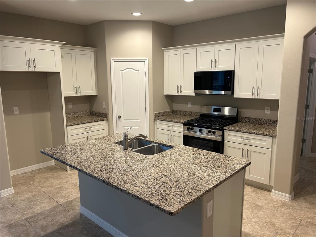 A kitchen features white cabinets, granite countertops, a central island, and stainless steel appliances — 720 E VICTORIA TRAILS BOULEVARD, DELAND, FL