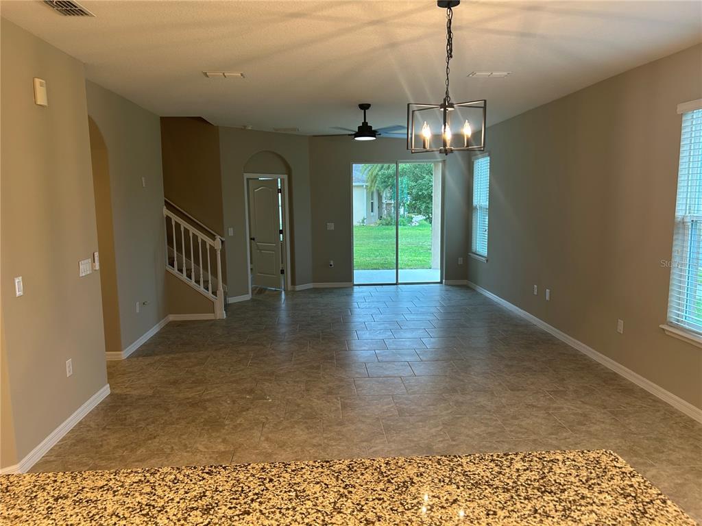 An open-concept living area features tile flooring, a staircase, and a sliding glass door — 720 E VICTORIA TRAILS BOULEVARD, DELAND, FL