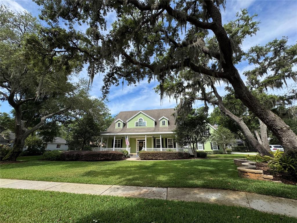 A light green two-story house with a wrap-around porch sits behind large oak trees — 2928 CHELSEA WOODS DRIVE, VALRICO, FL