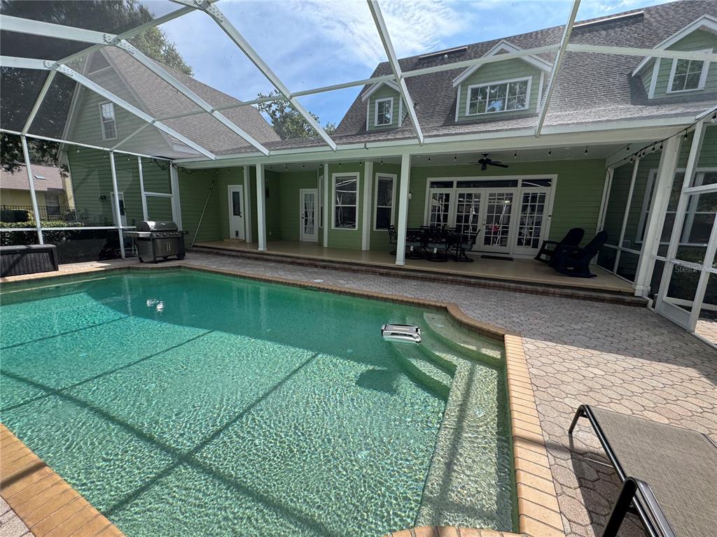 A screened-in swimming pool and patio area adjacent to a two-story green house — 2928 CHELSEA WOODS DRIVE, VALRICO, FL