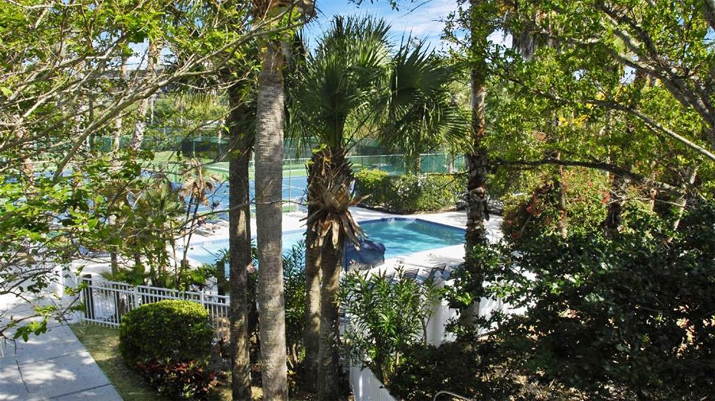 An outdoor swimming pool is surrounded by lush trees, palm trees, and a white fence — 1200 SIESTA BAYSIDE DRIVE UNIT 1200-G, SARASOTA, FL