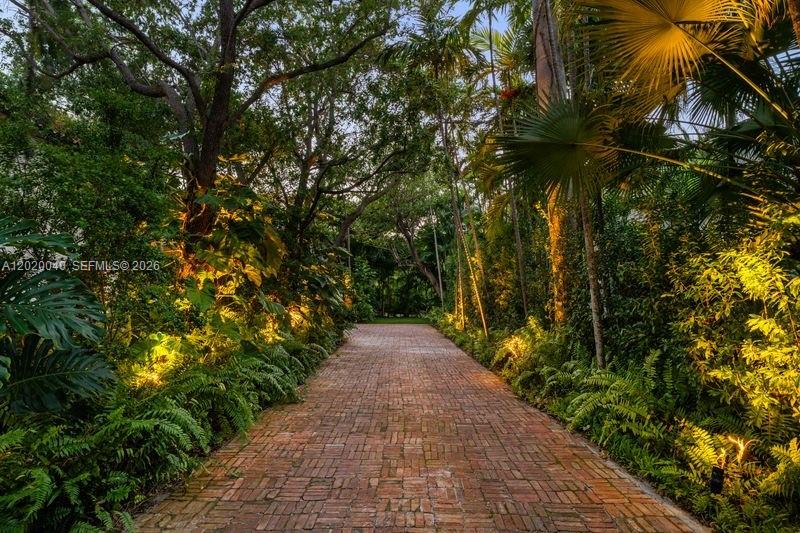 A brick driveway leads through a lush, tree-lined garden with landscape lighting — 5812 Alton Rd, Miami Beach FL 33140, MIAMI BEACH, FL