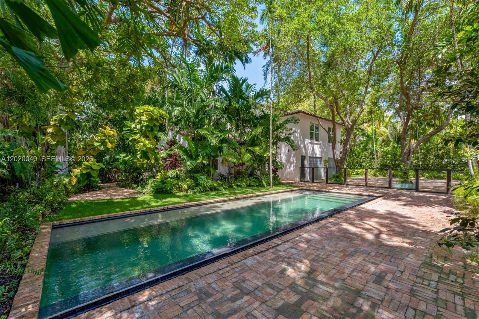 A rectangular swimming pool sits on a brick patio surrounded by lush trees and palms — 5812 Alton Rd, Miami Beach FL 33140, MIAMI BEACH, FL