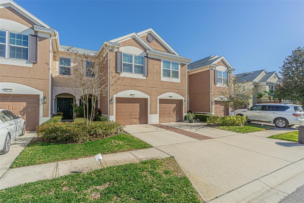 A row of tan townhouses with attached garages and driveways under a clear blue sky — 26544 CASTLEVIEW WAY, WESLEY CHAPEL, FL