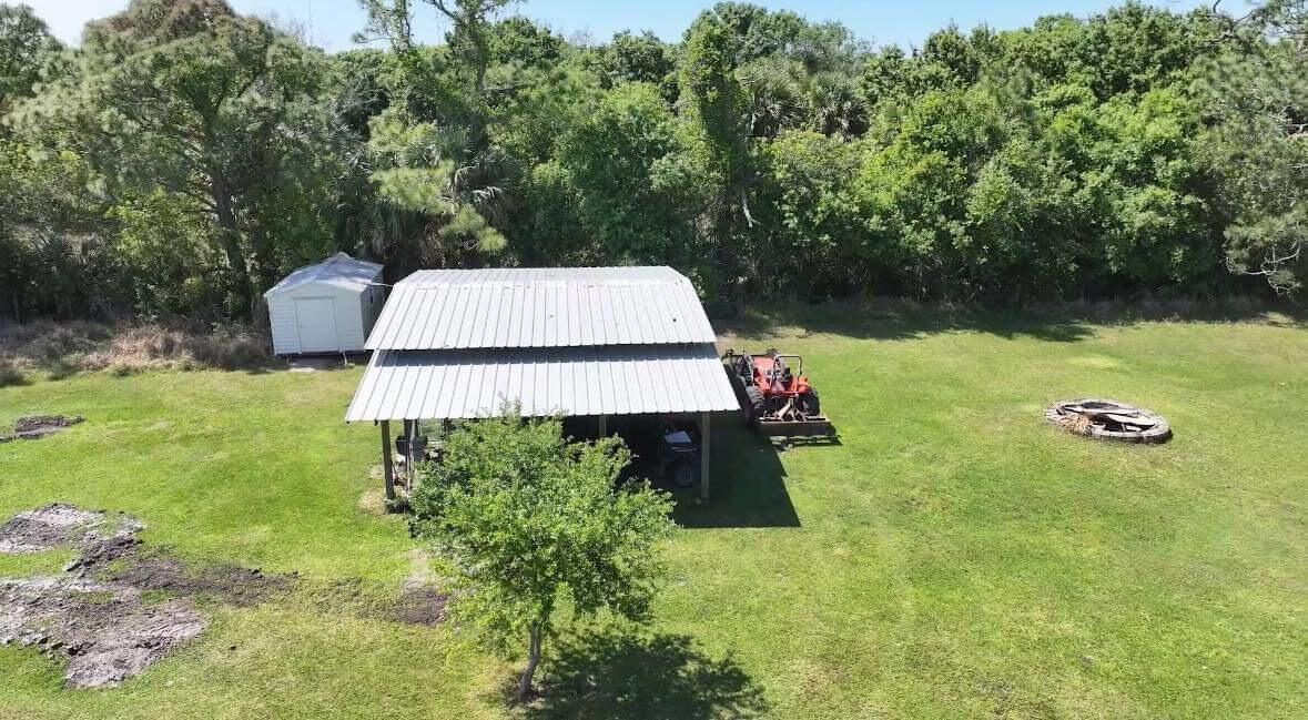 An aerial view shows a metal-roofed carport, a small shed, and a tractor on grass — 6045 21st Street SW, Vero Beach FL 32968, VERO BEACH, FL
