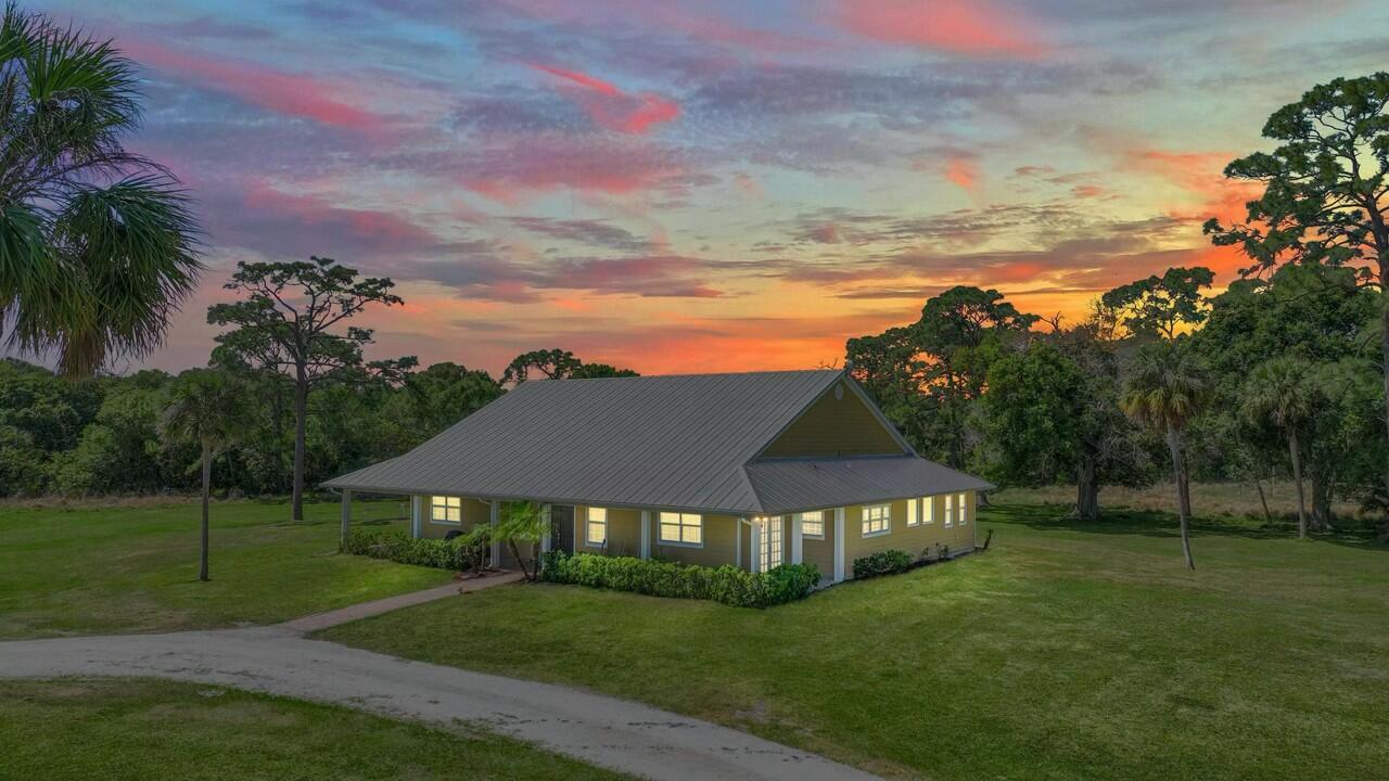 A single-story house with a metal roof sits on a grassy lot at sunset — 6045 21st Street SW, Vero Beach FL 32968, VERO BEACH, FL
