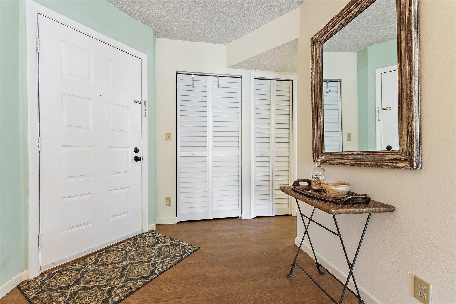 An entryway features a white front door, two louvered closets, wood flooring, and a mirror — 1605 S Us Highway 1 # B205, Jupiter FL 33477, JUPITER, FL