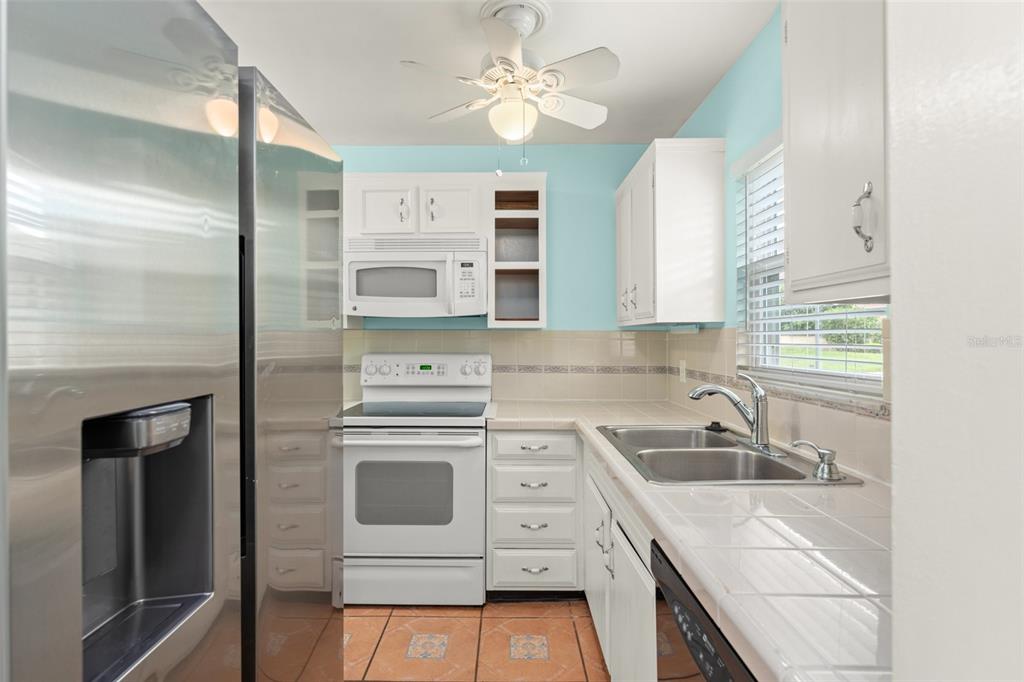 A kitchen features white cabinets, stainless steel appliances, tile countertops, and light blue walls — 1220 VILLA LANE UNIT 135, APOPKA, FL