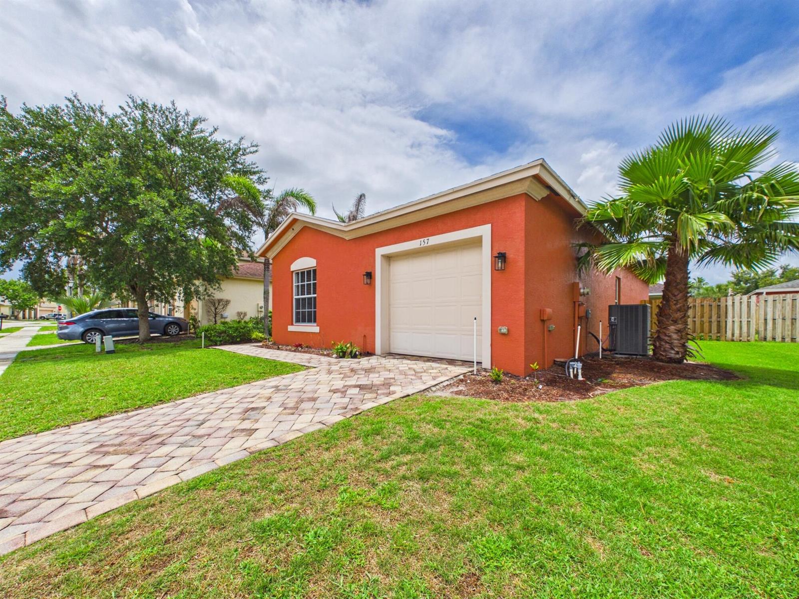 A single-story orange house with a paved driveway, a garage, and a palm tree — 157 Blue Grotto Drive, Fort Pierce FL 34945, FORT PIERCE, FL