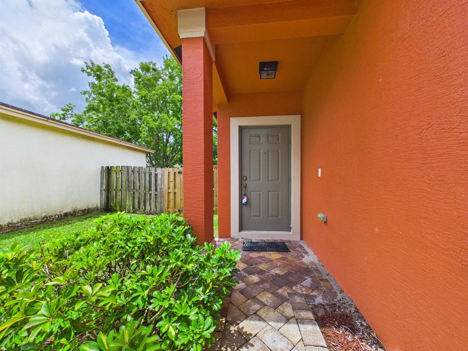 A covered entryway with a gray door, orange stucco walls, and a brick paver walkway — 157 Blue Grotto Drive, Fort Pierce FL 34945, FORT PIERCE, FL