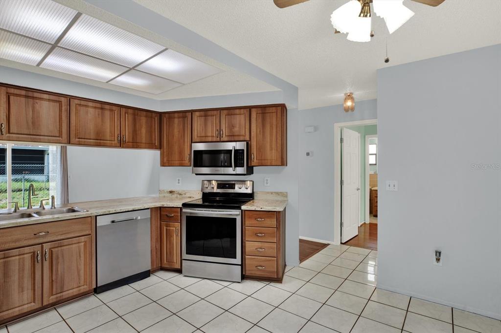 A kitchen features wood cabinets, stainless steel appliances, granite countertops, and white tile flooring — 8241 WINTHROP DRIVE, PORT RICHEY, FL