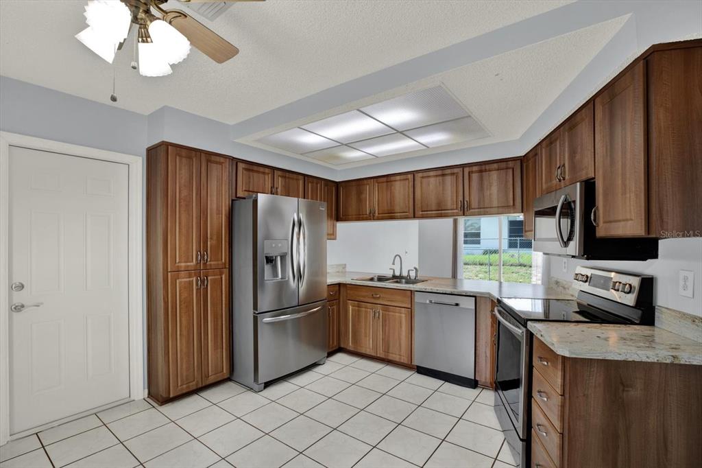 A kitchen features wood cabinets, stainless steel appliances, granite countertops, and white tile flooring — 8241 WINTHROP DRIVE, PORT RICHEY, FL