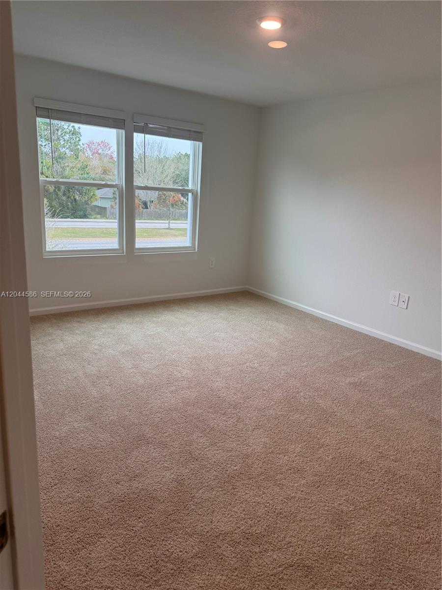 An empty bedroom features beige carpet, white walls, and two windows overlooking a street — 25 Redbud Rd, Palm Coast FL 32137, PALM COAST, FL