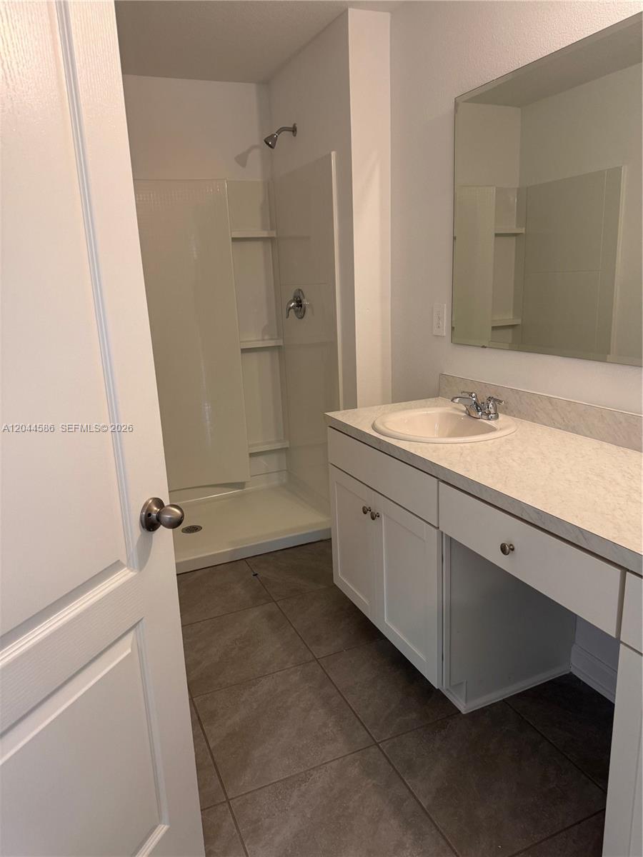A bathroom features a white vanity, a mirror, and a walk-in shower with tiled floors — 25 Redbud Rd, Palm Coast FL 32137, PALM COAST, FL