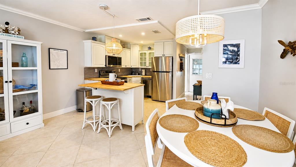 A kitchen and dining area featuring white cabinetry, stainless steel appliances, and a round table — 2750 OCEAN SHORE BOULEVARD UNIT 49, ORMOND BEACH, FL