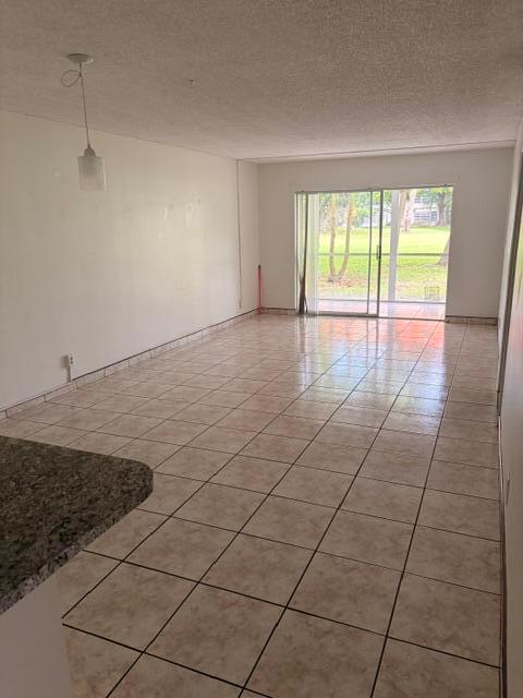 An empty living room features beige tile flooring, a pendant light, and sliding glass doors — 607 S State Rd 7 # 1g, Margate FL 33068, MARGATE, FL