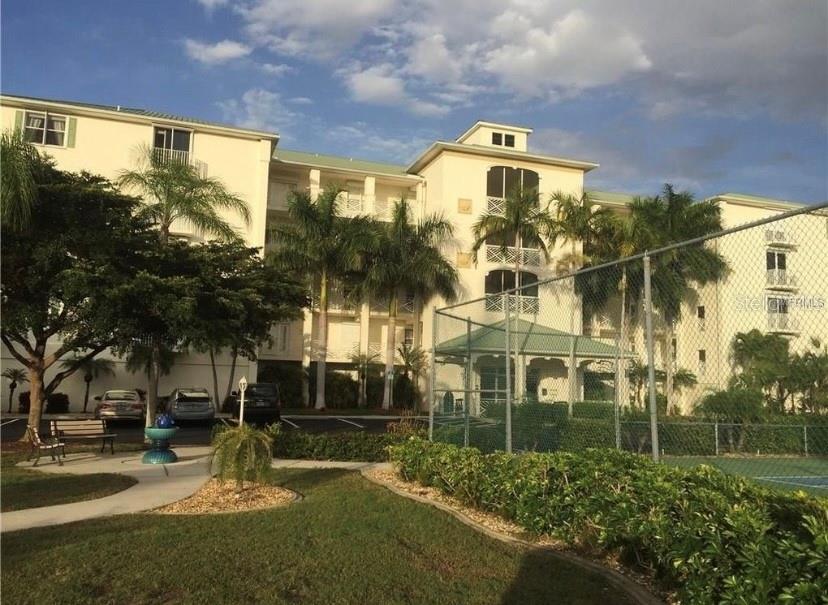 A multi-story beige apartment building stands behind a chain-link fence and a landscaped yard — 200 HARBOR WALK DRIVE UNIT 321, PUNTA GORDA, FL