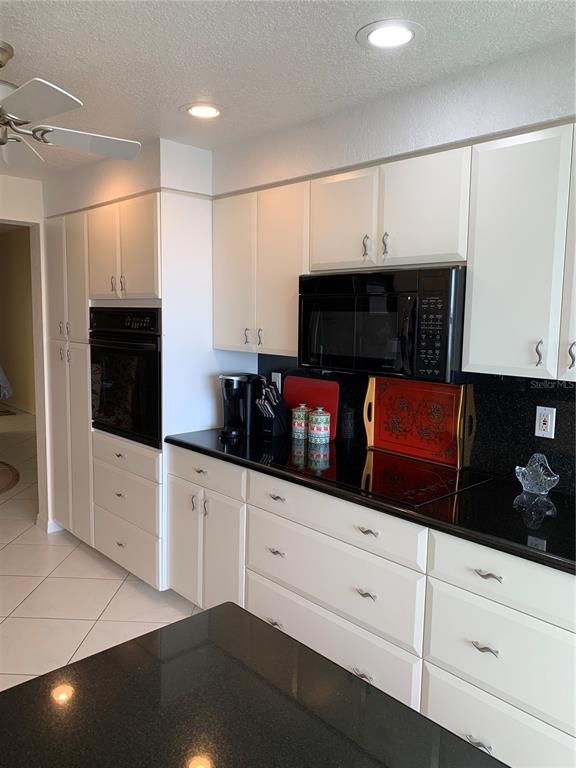 A kitchen features white cabinetry, black countertops, a built-in oven, and a microwave — 200 HARBOR WALK DRIVE UNIT 321, PUNTA GORDA, FL