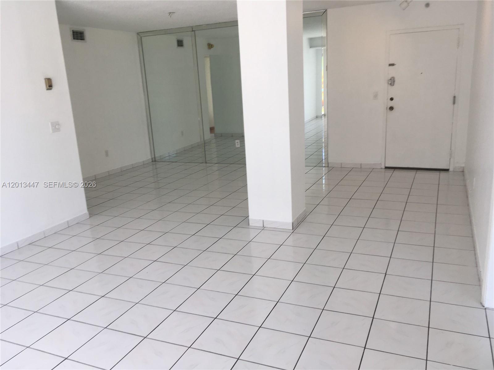 An empty room features white tiled floors, a central structural pillar, and mirrored closet doors — 77 Crandon Blvd # 2E, Key Biscayne FL 33149, KEY BISCAYNE, FL