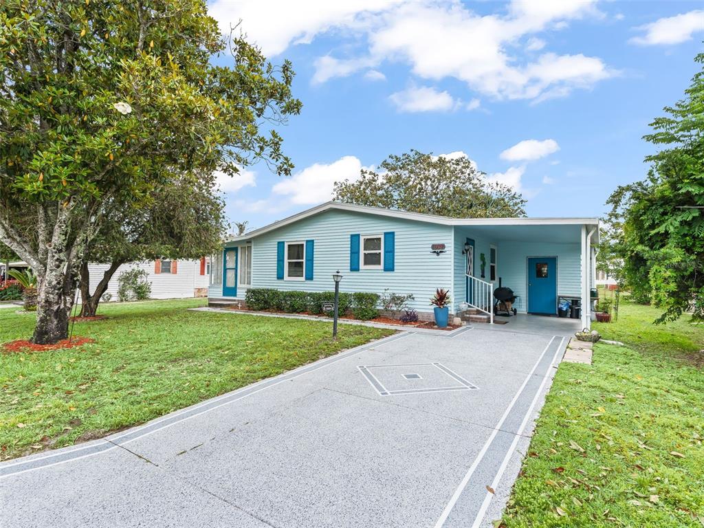 A light blue single-story house with a carport and a paved driveway sits on grass — 1809 DAFFODIL LANE, LADY LAKE, FL