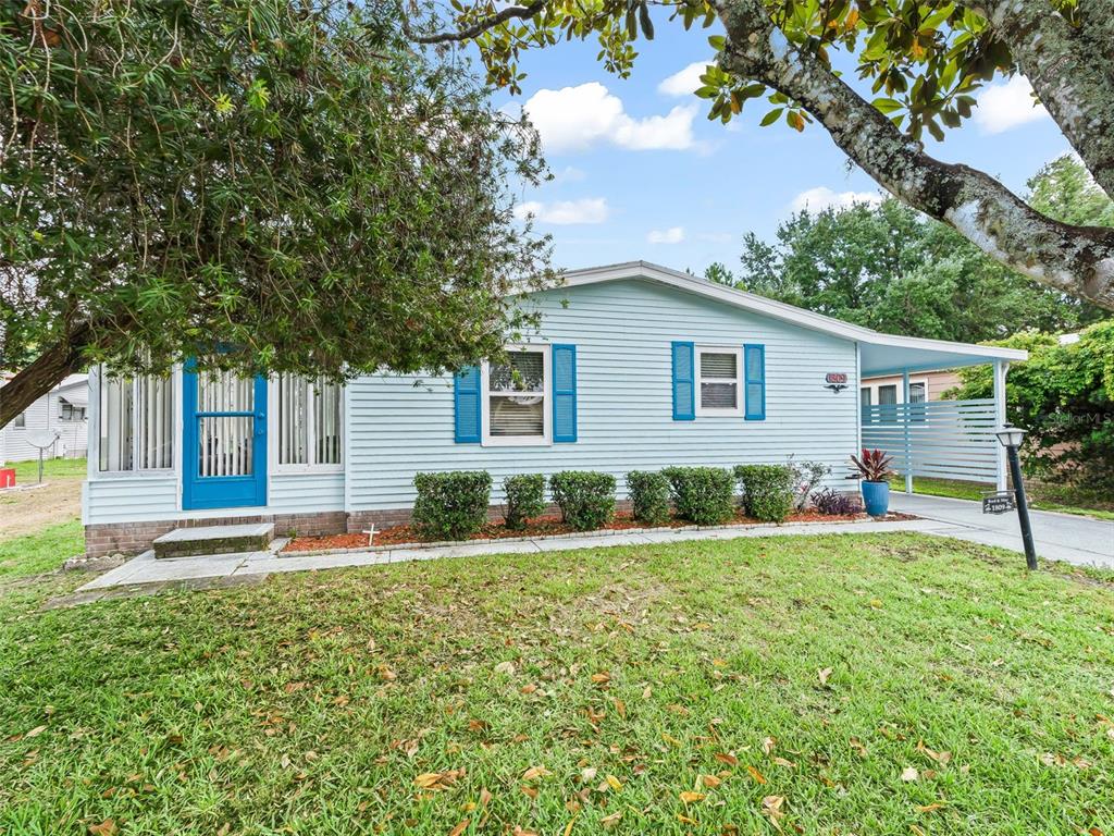 A light blue house with blue shutters, a front porch, and a carport — 1809 DAFFODIL LANE, LADY LAKE, FL