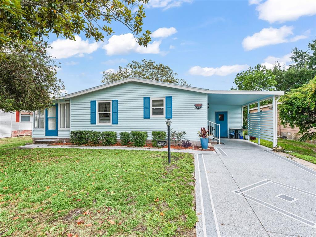 A light blue single-story house features a front carport, blue shutters, and a concrete driveway — 1809 DAFFODIL LANE, LADY LAKE, FL