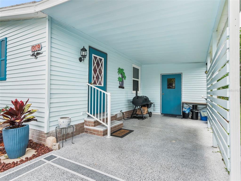 A light blue house exterior features a covered carport, two blue doors, and a grill — 1809 DAFFODIL LANE, LADY LAKE, FL
