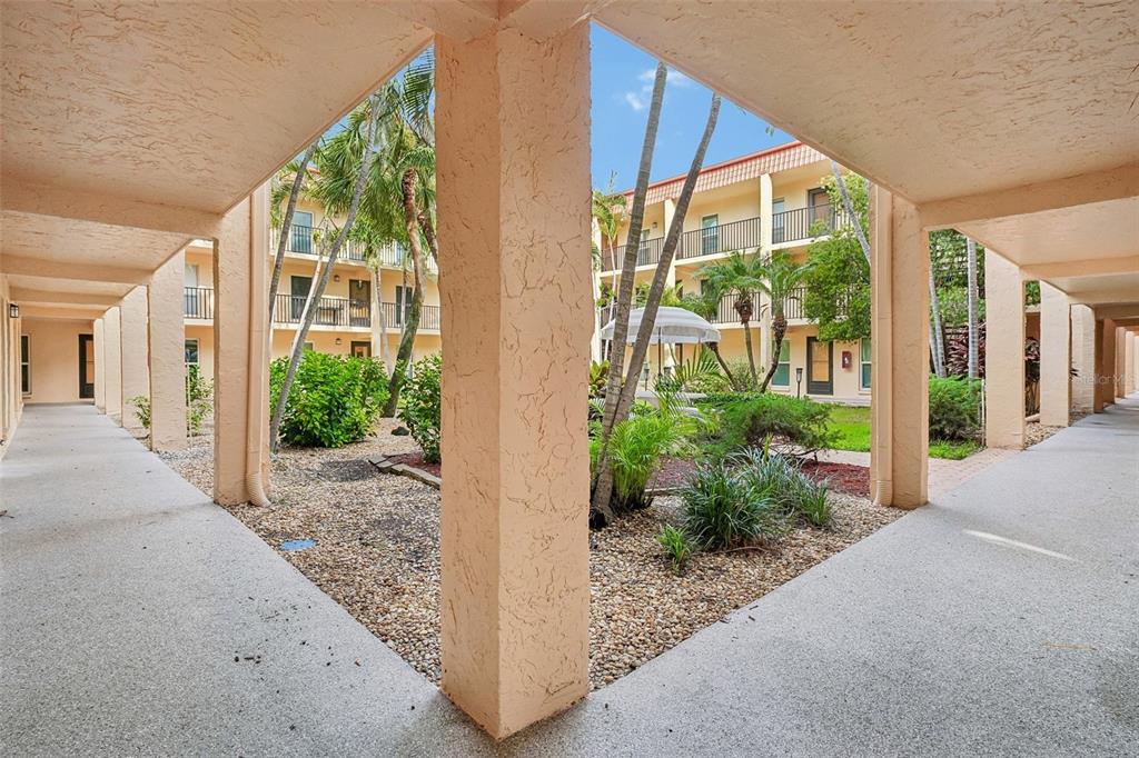 A view from a covered walkway looking out toward a landscaped courtyard with palm trees — 8911 BLIND PASS ROAD UNIT 104, ST PETERSBURG, FL