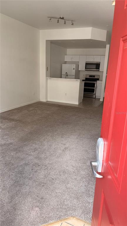 A view from a red doorway into a carpeted living area with an open kitchen — 2608 LODI CIRCLE UNIT 103, KISSIMMEE, FL