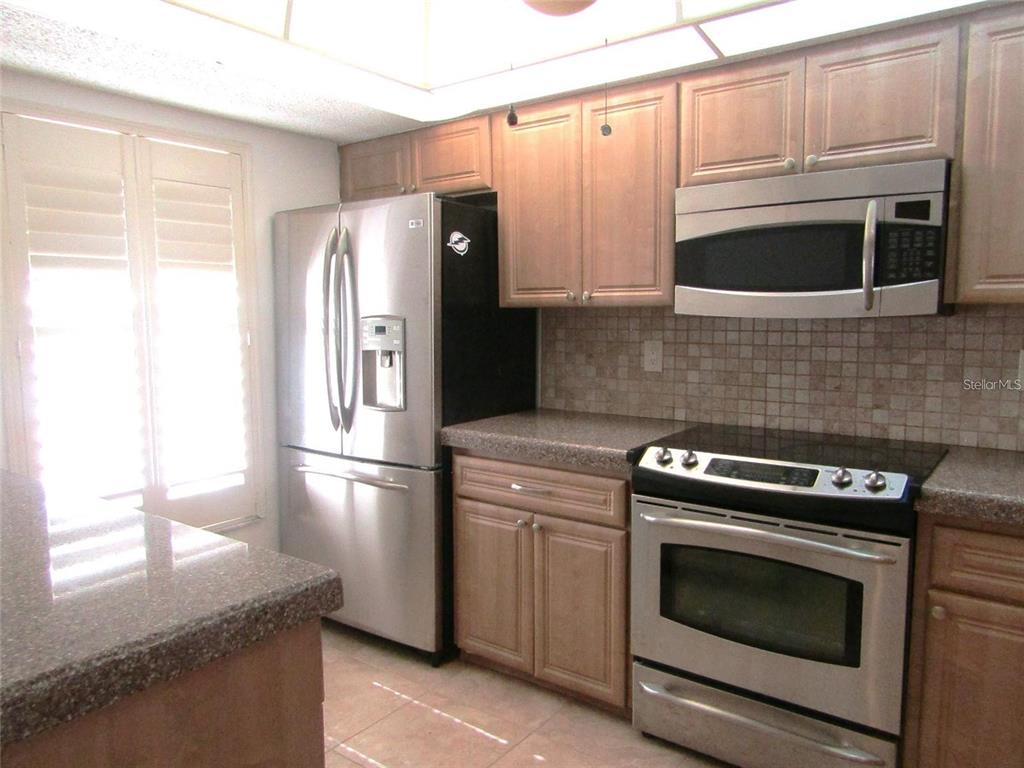 A kitchen featuring light wood cabinets, stainless steel appliances, and a tiled backsplash — 4434 WEYBRIDGE UNIT 81, SARASOTA, FL