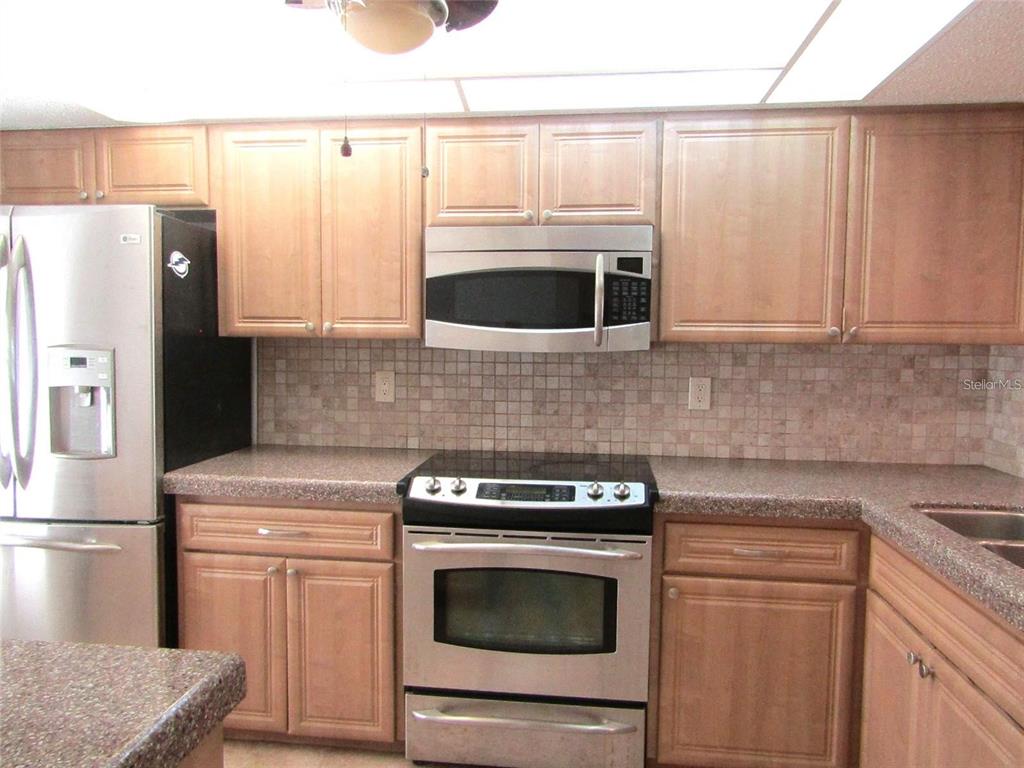 A kitchen features light wood cabinets, stainless steel appliances, and a tiled backsplash — 4434 WEYBRIDGE UNIT 81, SARASOTA, FL