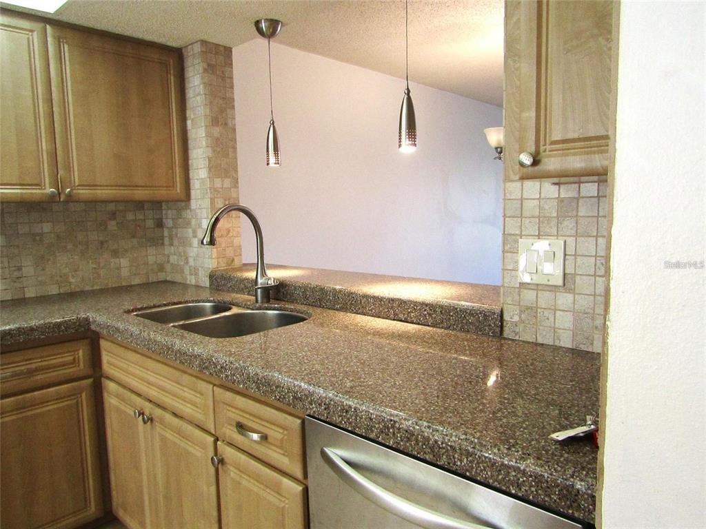 A kitchen features wood cabinets, speckled countertops, a double sink, and two pendant lights — 4434 WEYBRIDGE UNIT 81, SARASOTA, FL