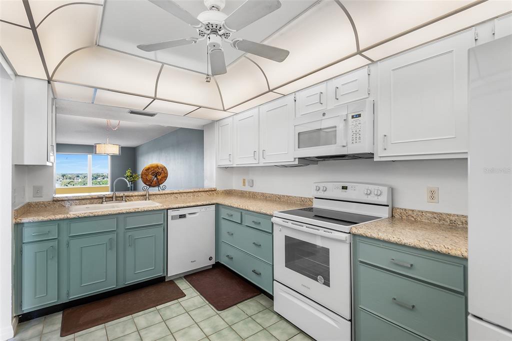 A kitchen features white upper cabinets, blue lower cabinets, granite countertops, and a ceiling fan — 1776 6TH STREET NW UNIT 807, WINTER HAVEN, FL