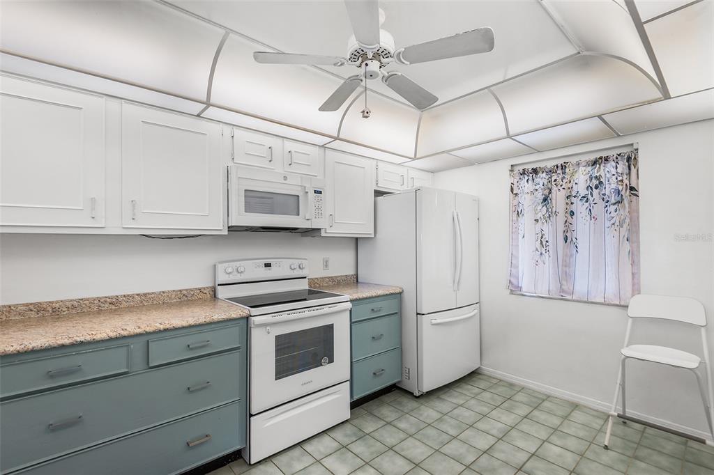 A kitchen features white upper cabinets, blue lower cabinets, granite countertops, and a ceiling fan — 1776 6TH STREET NW UNIT 807, WINTER HAVEN, FL