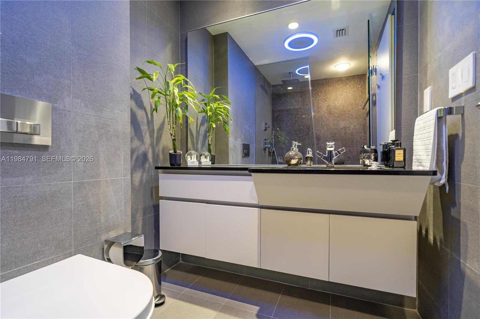A modern bathroom features a floating white vanity, gray tiled walls, and a large mirror — 2627 S Bayshore Dr # 1408, Miami FL 33133, MIAMI, FL