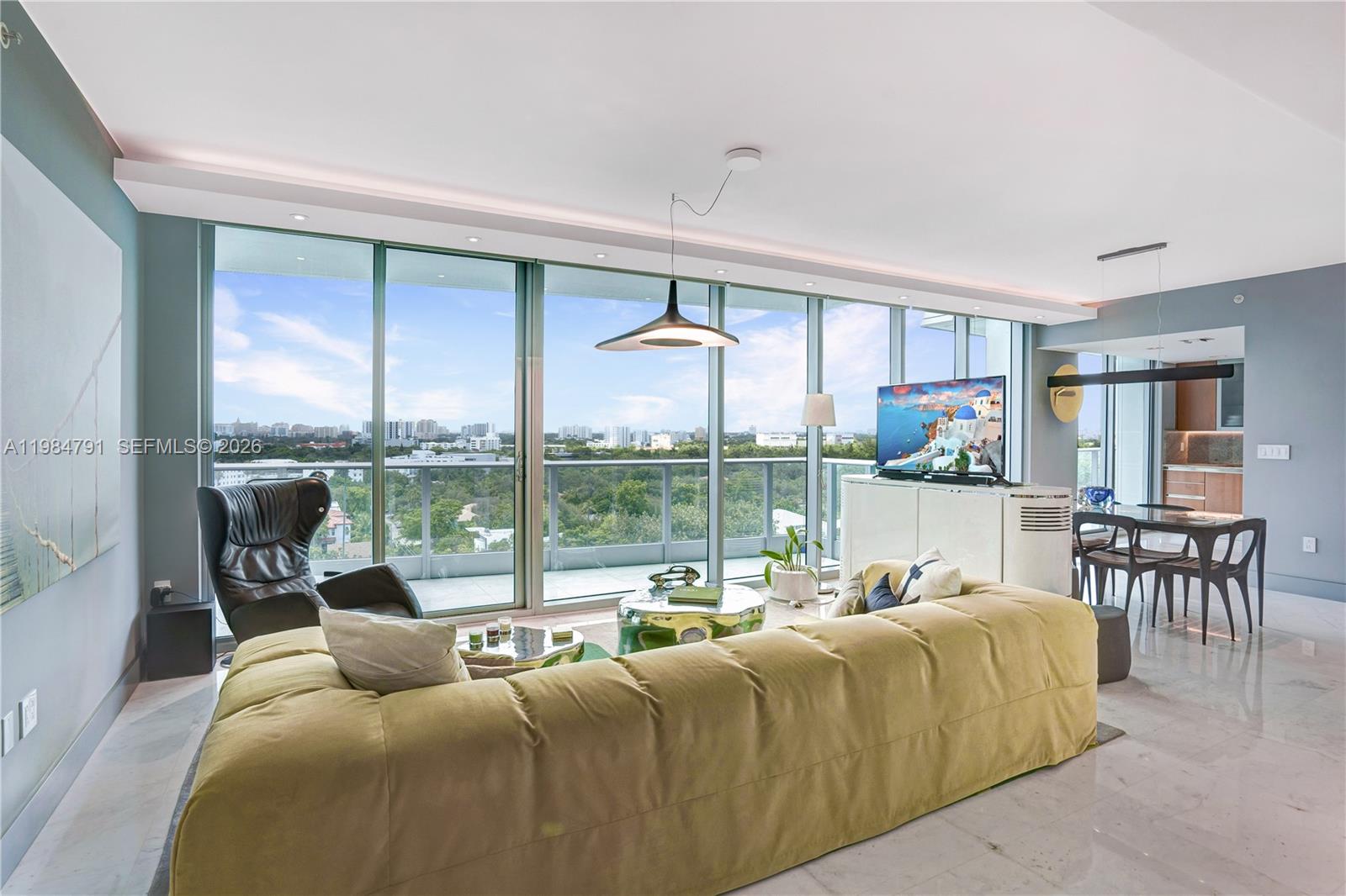 A living room features a large yellow sofa, floor-to-ceiling windows, and a city view — 2627 S Bayshore Dr # 1408, Miami FL 33133, MIAMI, FL