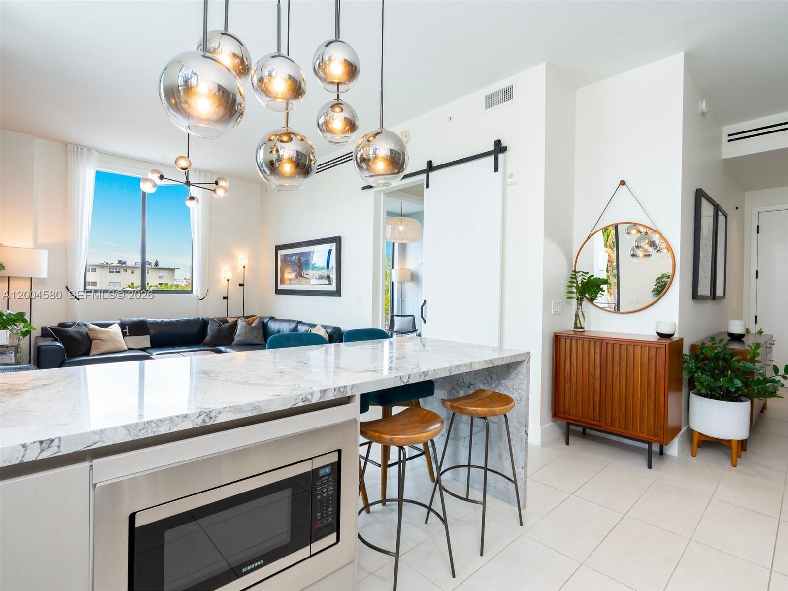 A modern kitchen with a marble waterfall island, pendant lighting, and an adjacent living area — 1030 15th St # 321, Miami Beach FL 33139, MIAMI BEACH, FL