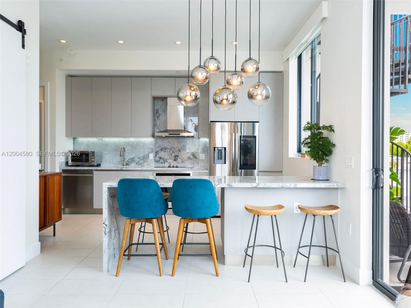 A modern kitchen features gray cabinetry, marble countertops, blue velvet stools, and a pendant light fixture — 1030 15th St # 321, Miami Beach FL 33139, MIAMI BEACH, FL