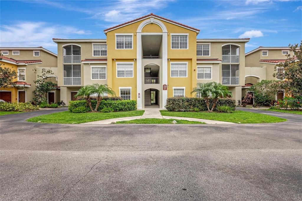 A three-story apartment building with a yellow facade, arched entryway, and screened balconies — 5500 BENTGRASS DRIVE UNIT 6-301, SARASOTA, FL