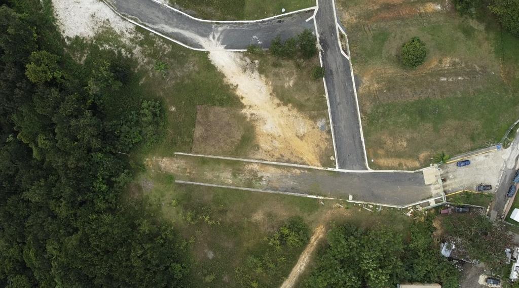 An aerial view shows a paved road extending into a grassy, undeveloped residential lot — HACIENDA RIO LAJAS UNIT #1, DORADO, PR